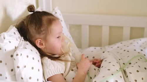 L'enfant est allongé dans son lit sous une couverture à pois et respire dans un masque nébuliseur pour inhalation