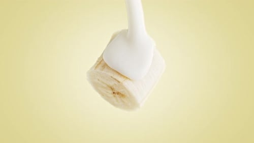 Yogurt Pouring from Top over a Banana on Yellow Background in Slow Motion and Macro