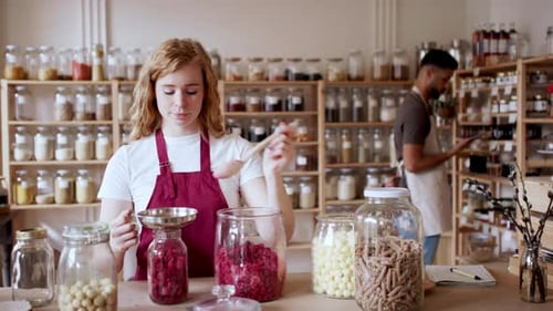 Young woman fills jar with raspberries at sustainable zero waste shop