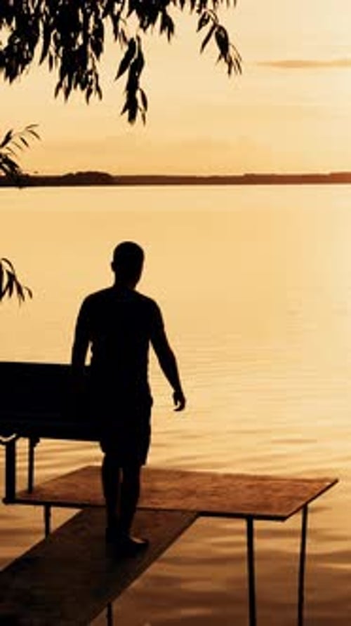 A young man goes to the bridge on the river and looks on a beautiful view of the sunset.
