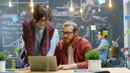 Dois designers criativos olham para o laptop e têm grande sucesso. Eles fazem High Five e riem. Em t