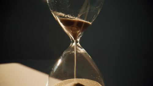 Granos de arena dorada que corren dentro de un reloj de arena midiendo el tiempo en la cuenta regresiva de cerca