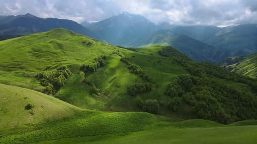 Cloudy Sky Over Lush Green Mountain Slope with Grass and Trees