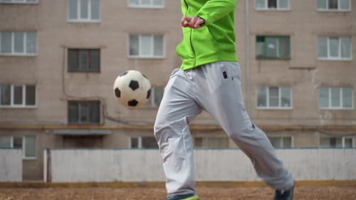 Fullbody Control and Run with Soccer Ball Near Apartment Blocks Player in Green Hoodie and Beanie