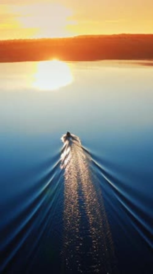Aerial view of landscape during sunset. Camera follows the boat sailing on the river