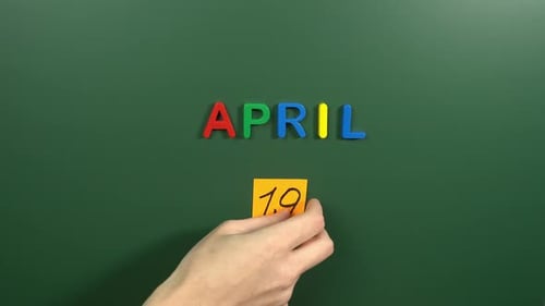 Hand sticking a sticker 19 April calendar day on school board. 19 date of April. Nineteenth day