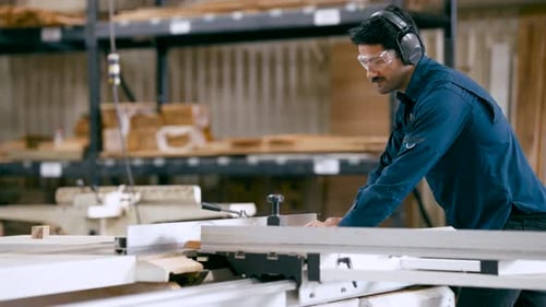 Man Cutting Wood on Saw in Workshop