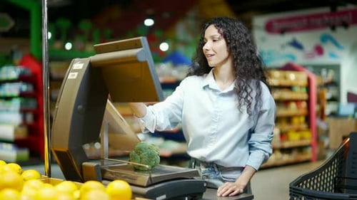 young pretty brunette woman shopper weighs groceries vegetables in supermarket grocery store Female