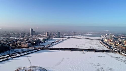 Drone backwards shot over iced and snowy Daugava River in Riga City with bridges and buildings