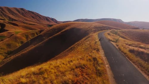 Locals Walking Along a Winding Road Traverse the Dry Golden Hills of Madagascar with Distant