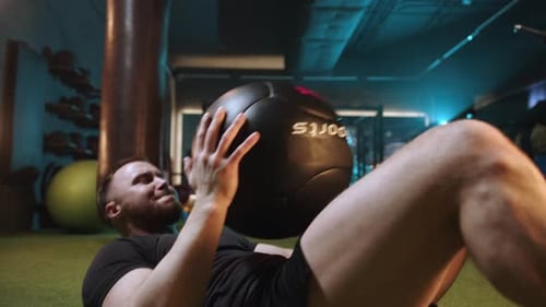 A Focused Man is Engaged in Rigorous Exercise Using a Medicine Ball at a Contemporary Gym