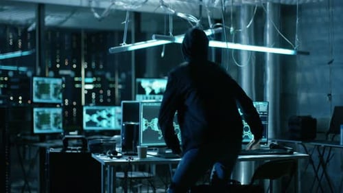 Hooded Hacker Takes His Place in at His Desk in Hacker's Den. Place is Neon, Dark and Has Many Disp