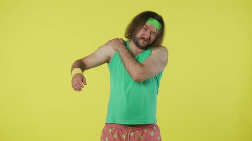 Man in Green Top and Headband Feeling Pain in the Shoulder Doing Warm Up Isolated on Yellow