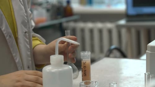 Ajouter soigneusement un solvant transparent dans un flacon rond au-dessus d'un bécher dans un environnement de laboratoire bien éclairé