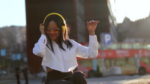 African american woman listening to music with headphones at sunset in the city, music online and da
