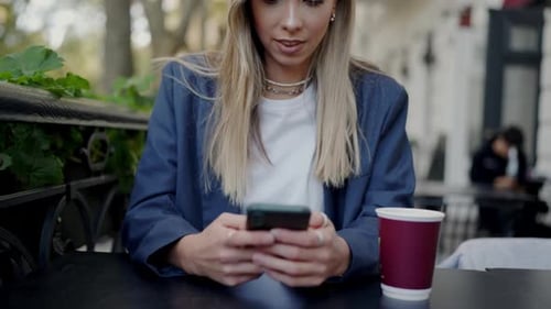 Businesswoman Texting Outdoors at Cafe with Coffee on Table
