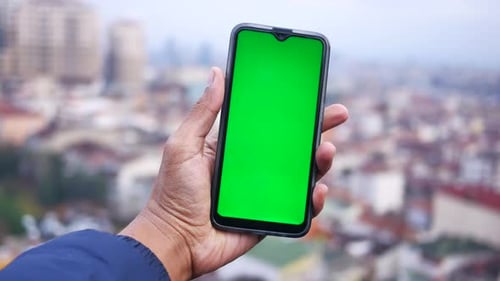 Young Man Hand Using Smart Phone with Green Screen Against City Buildings