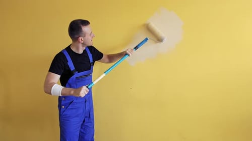 Zimmerrenovierungen zu Hause. Der Maler fängt an, die Wand mit einer Rolle an einem langen Griff zu streichen.