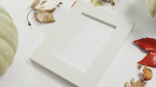 Empty frame with copy space, pumpkin and autumn leaves against white background
