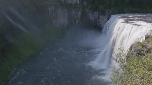 Wide view of a large waterfall is seen flowing with mist rising from the bottom.