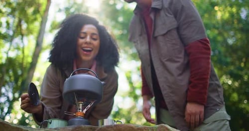 Woman Makes Tea on Camp Stove with Man Nearby