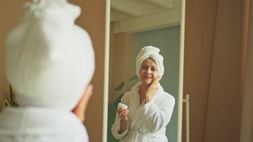 Senior Woman Applies Cream in the Mirror