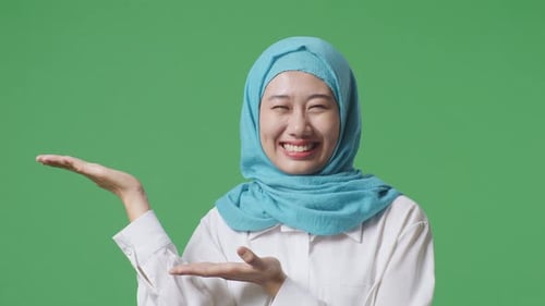 Close Up Of Asian Muslim Woman Smiling And Pointing To Side While Standing In The Green Screen