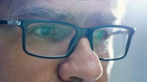 Nahaufnahme eines älteren Mannes mit Brille und Computerbildschirm spiegelt sich in ihnen wider.