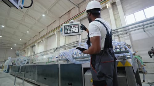 Factory Worker in a Hard Hat and Uniform is Using a Tablet with an Engineering Software