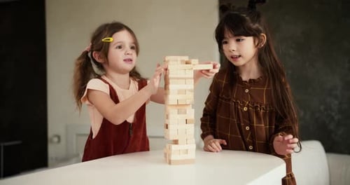 Two Preteen Girls Friends Children Playing Board Game Jenga on Table in Kitchen at Home Slow Motion