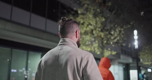 A Young Man with a Stylish Trendy Hairstyle and Beard in Casual Clothes Stands on a Night City