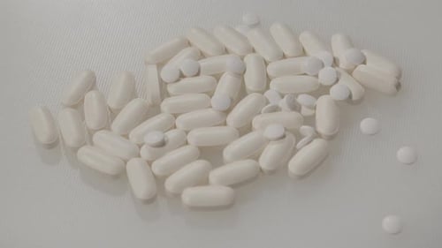White Pills and Capsules Poured on White Background