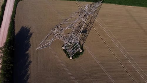 aerial close up of high voltage pylon for electricity transportation in the middle of a plowed field