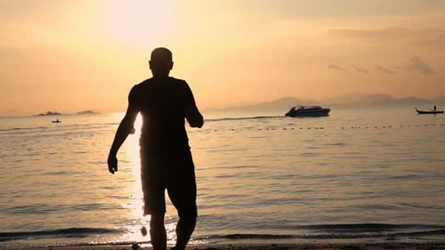 Silhouette of a lone man walking on a golden beach at sunset in super slow motion