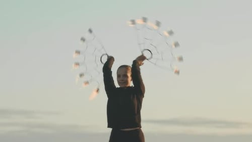 Girl Dancing with Fire Fans in Field at Sunset