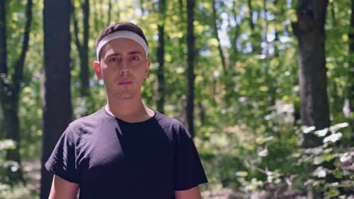 Running training program in a forest setting. A man runs in the park, smiles at the camera, enjoying