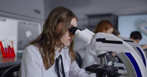 Jugendliches Mädchen schaut ins Mikroskop im Biologieunterricht im modernen Schulporträt