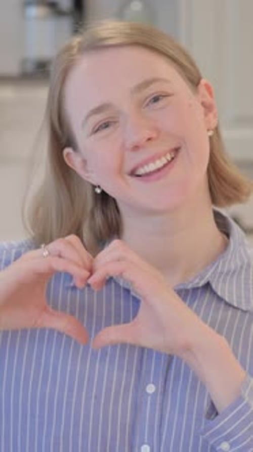 Smiling Woman Makes Heart Shape with Hands at Home