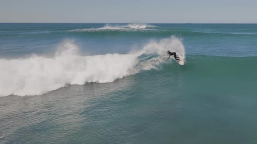 Surfer man riding the perfect deep blue ocean wave on a cloudless sunny day