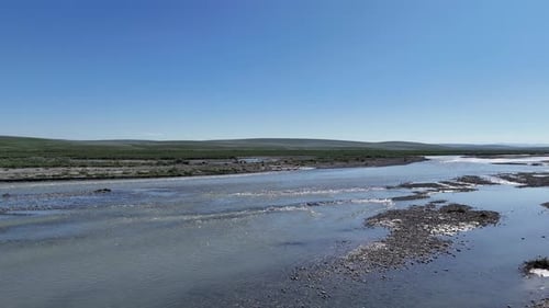 Panning scenic view of a wide, shallow river flowing through a vast, treeless tundra landscape