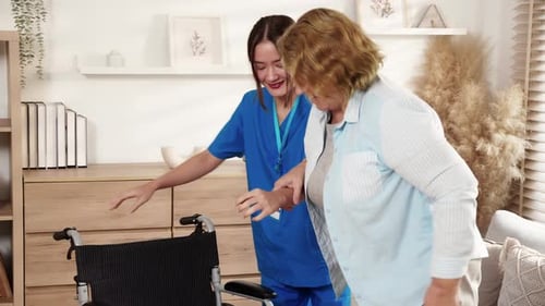 Nurse Assists Senior Woman into Wheelchair at Home