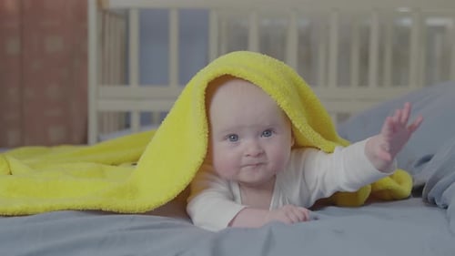 Baby Lying on Bed with Yellow Towel on Head