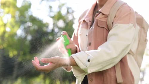 Woman spraying tick repellent onto hand in park, closeup