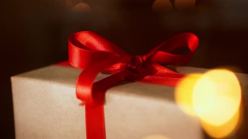 Close up Christmas gift craft paper box with red ribbon bow over dark lights bokeh background. New y