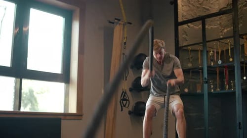 Handsome Fitness Man Training In Sport Club. Focused Bodybuilder Using Battle Ropes At Gym. Stron...
