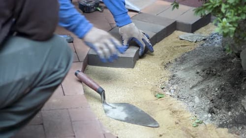 Closeup of putting brick pavers in place along an edge of a rock wall.