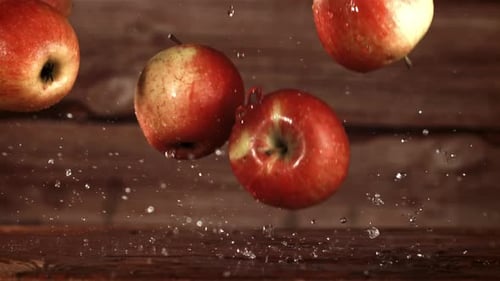 Red Apples Falling onto Wet Wooden Surface
