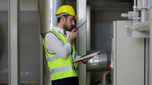 Männlicher 4K-Ingenieur, der auf dem Werksgelände am Walkie-Talkie arbeitet und spricht.
