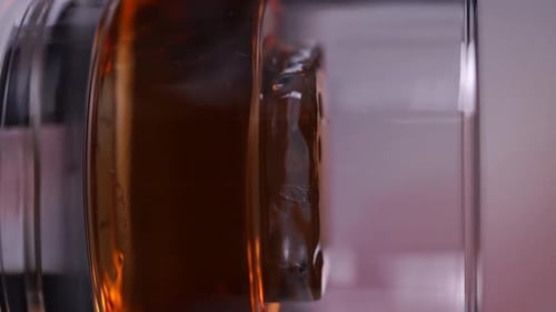 Glas Whiskey mit einem Eiswürfel, der sich auf einer kreisförmigen Plattform dreht