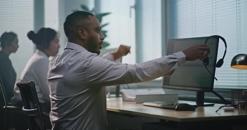 Afroamerikanischer Berater setzt sich an den Computer, setzt Headset auf, benutzt Computer